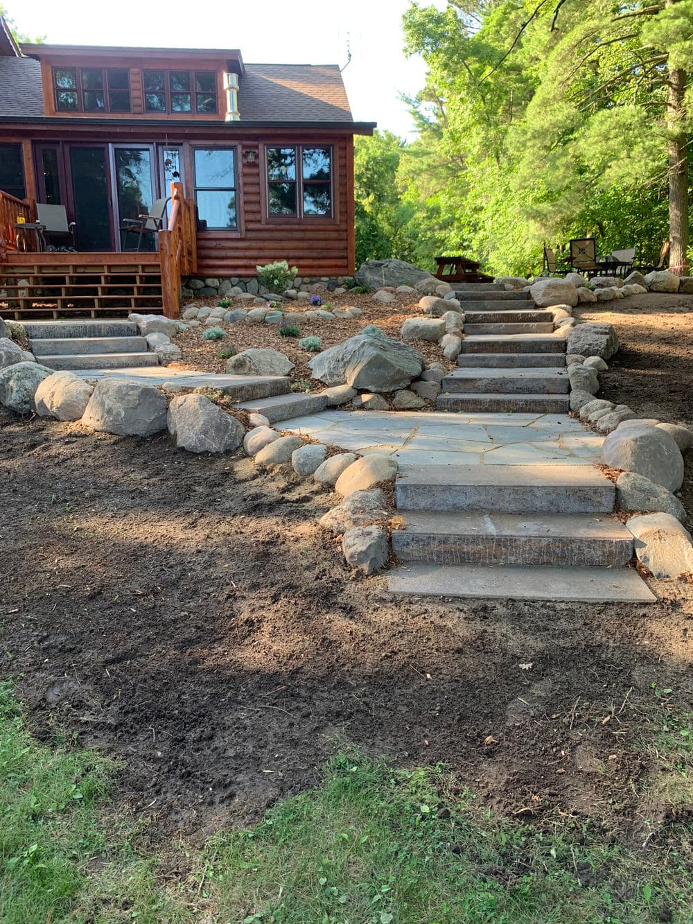 Log cabin home with stone pathway and landscaped garden in a lush green setting.