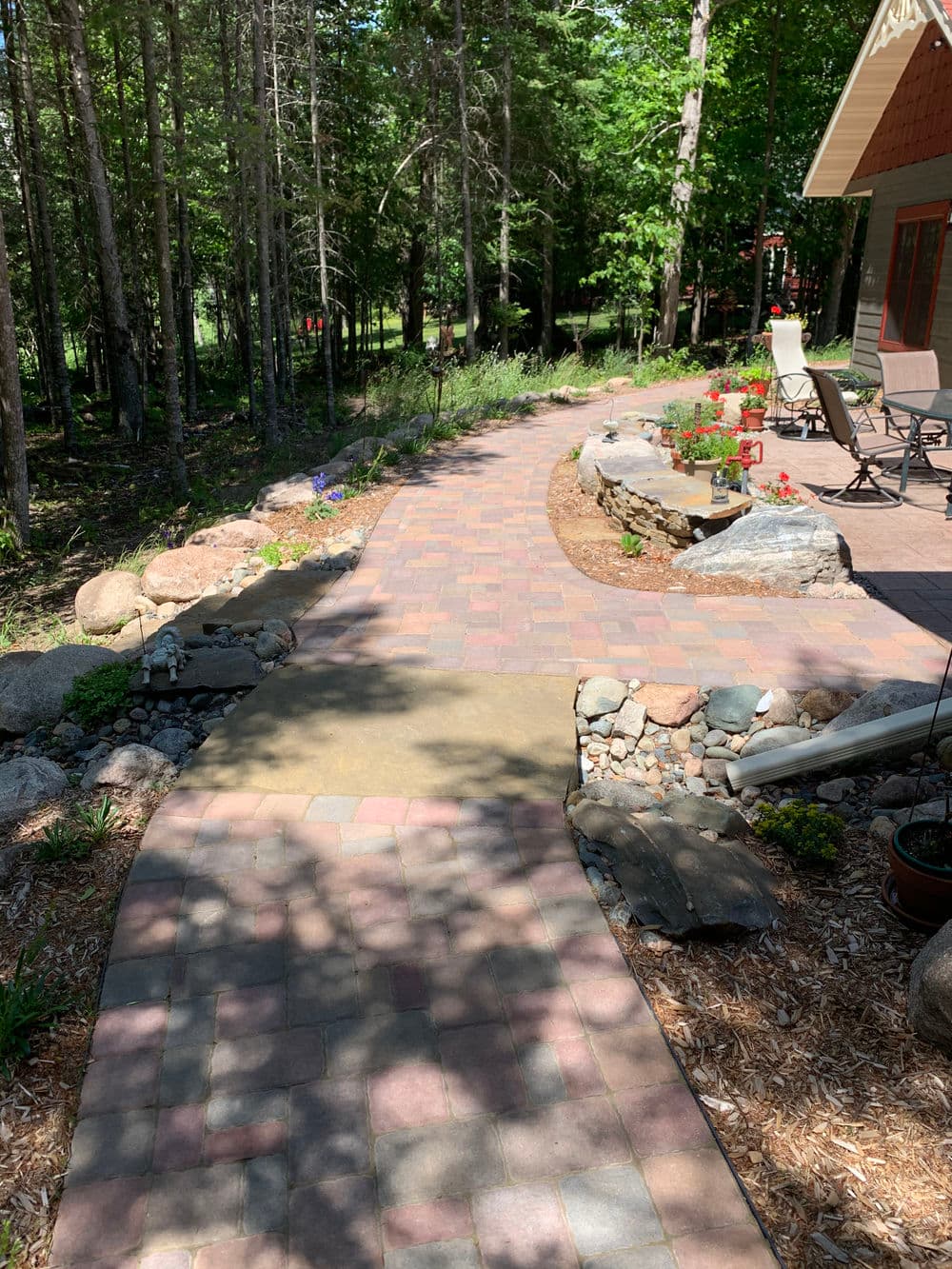 Scenic garden pathway with stone borders, surrounded by greenery and flowering plants.