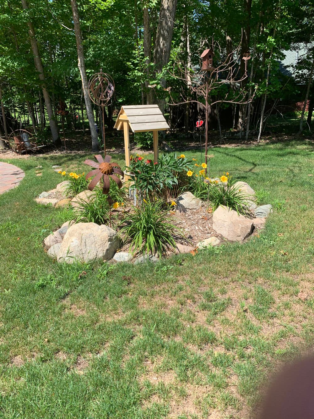 Colorful garden with birdhouse, flowers, and decorative windmill surrounded by rocks.
