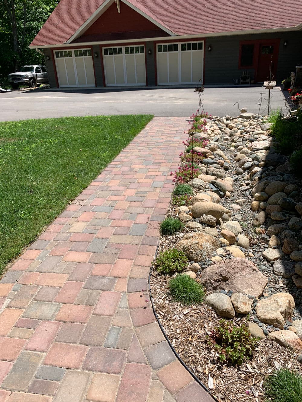 Brick walkway leading to a modern home with a landscaped yard and stone features.