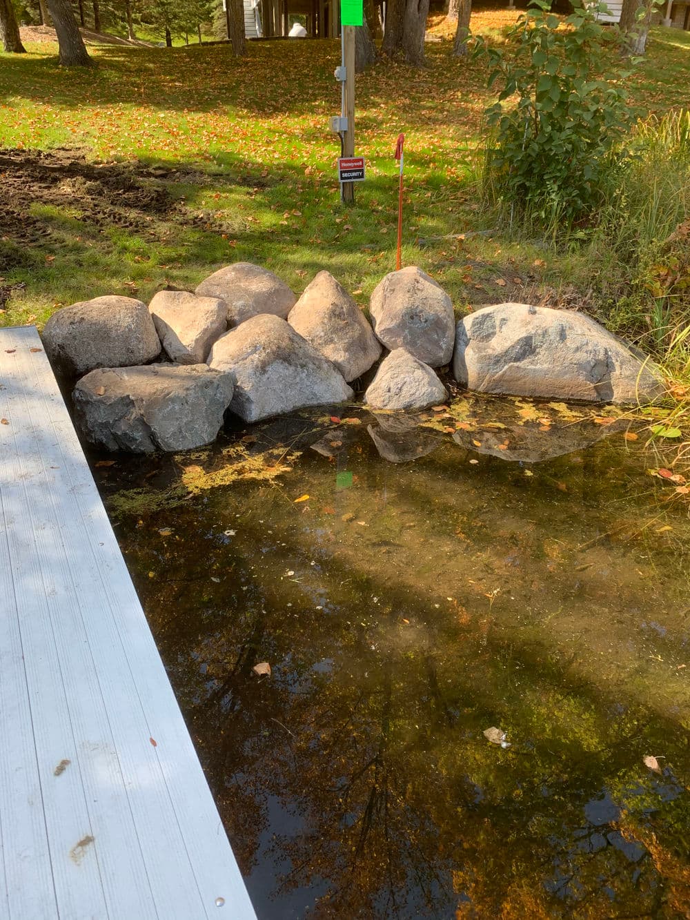 Rock barrier by a serene lake, surrounded by autumn leaves and lush greenery.