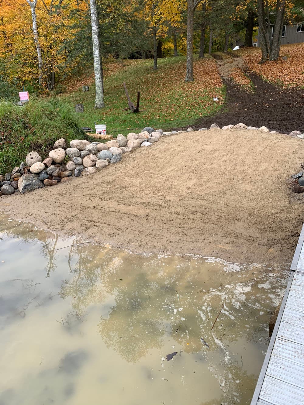 Sand beach area by a lake, surrounded by rocks and autumn foliage. Ideal for outdoor activities.