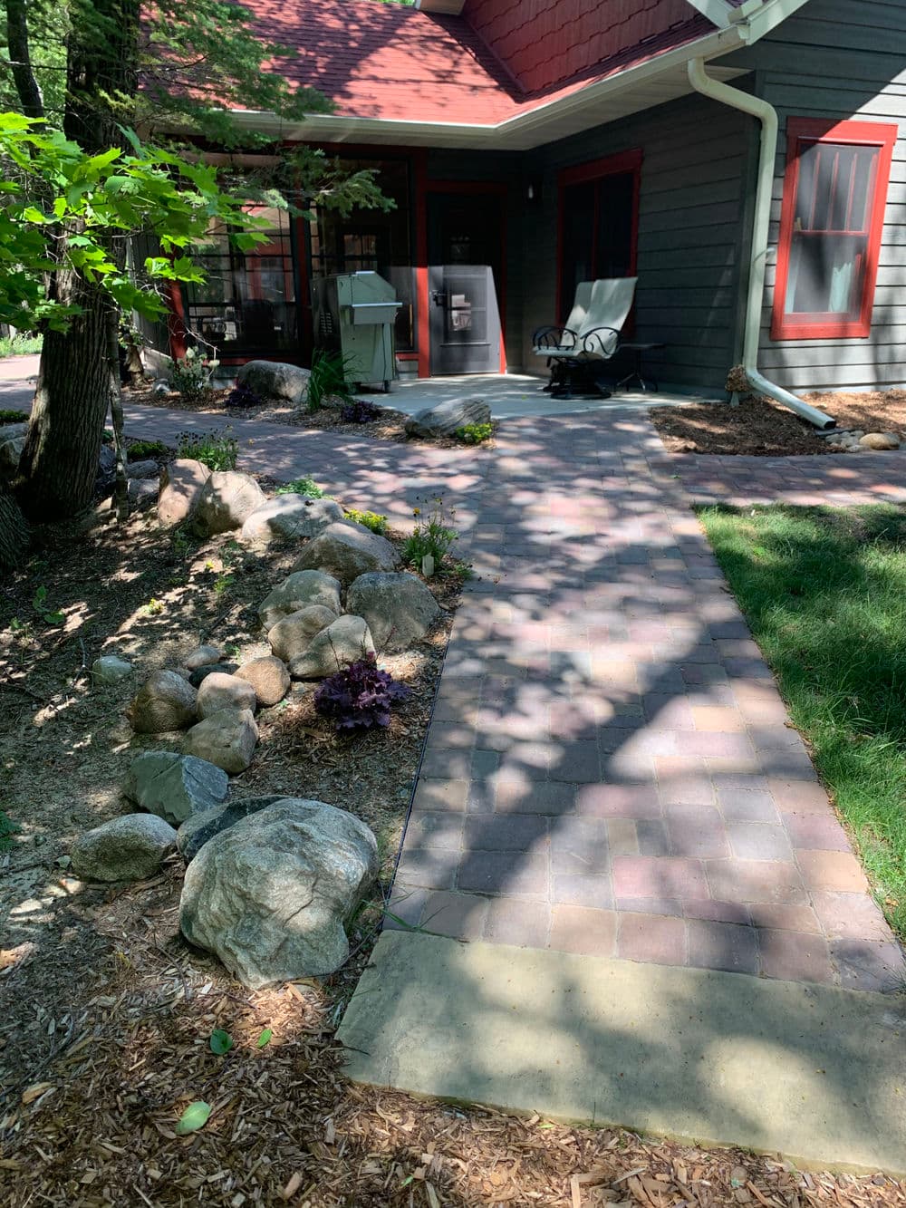 Pathway with stone borders leading to a home with a shaded porch and lush greenery.