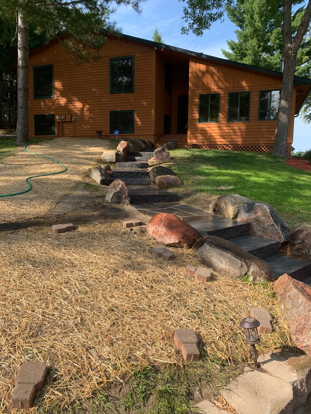 Modern wooden house with stone path and water feature in a landscaped garden.