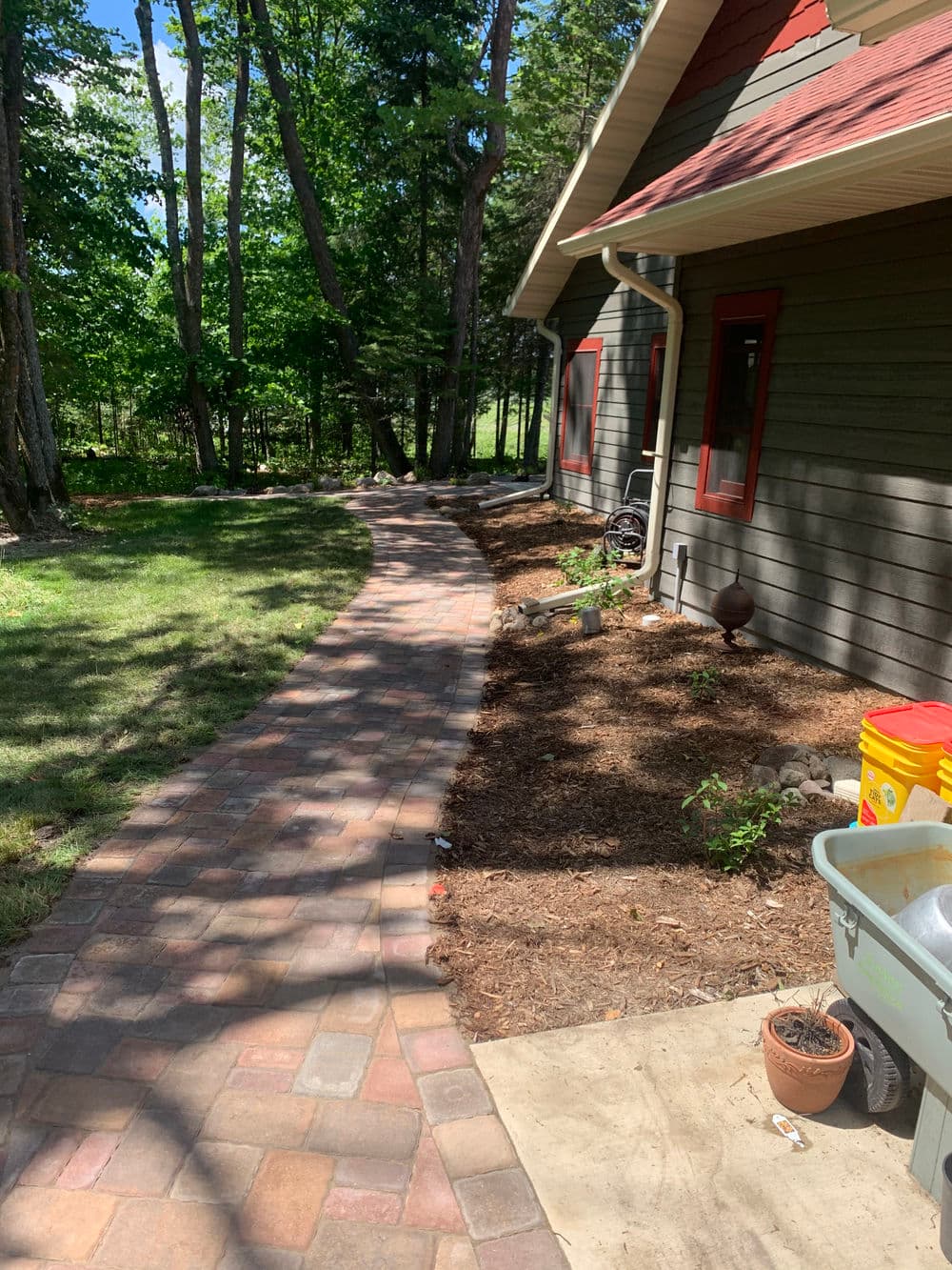 Curved brick walkway leading to a house surrounded by trees and mulch landscaping.