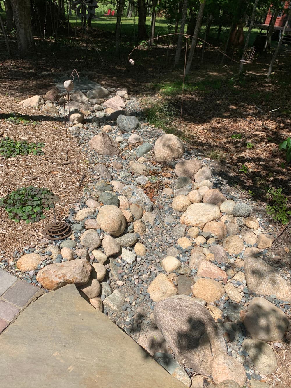 Landscaped stone pathway in a garden, featuring various sizes of smooth rocks and greenery.
