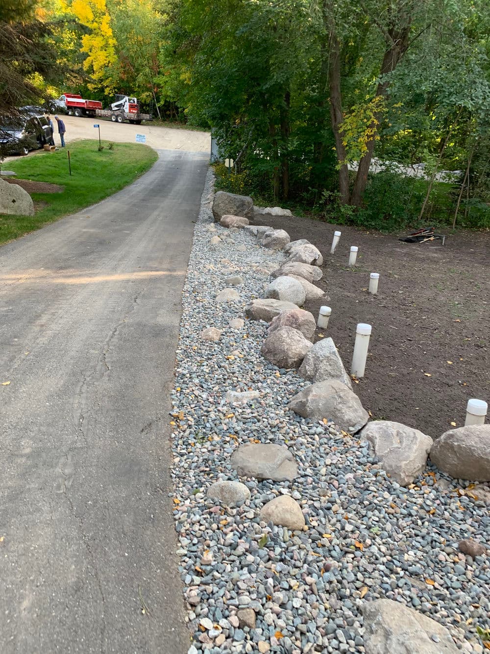 Gravel-lined driveway with large rocks and green trees, enhancing outdoor landscaping.