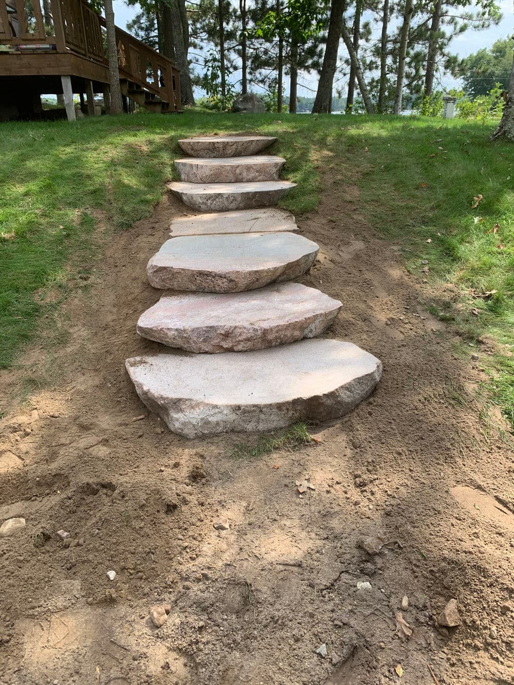 Stone steps leading up a grassy hillside, surrounded by trees and a dirt pathway.