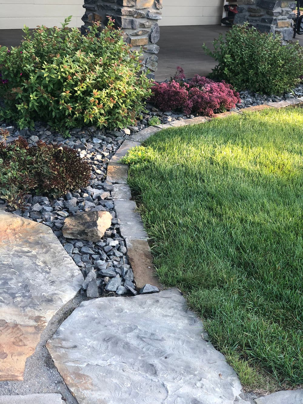 Landscaped pathway with stone, gravel, and colorful shrubs in a residential garden setting.