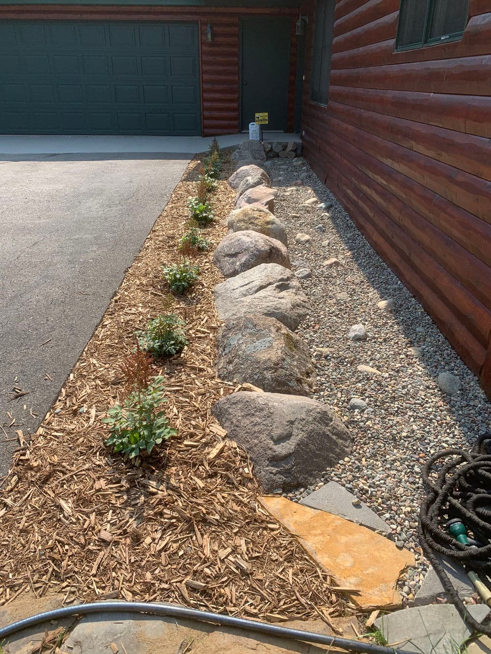 Landscaped garden with large rocks, gravel, and plants along a house's side pathway.