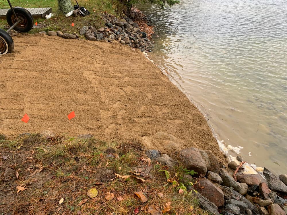 Sandy shoreline preparation with flags, rocks, and water in background. Ideal for landscaping.