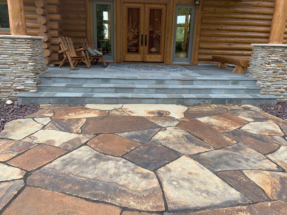 Log cabin entrance featuring a stone walkway, wooden chairs, and a welcoming atmosphere.