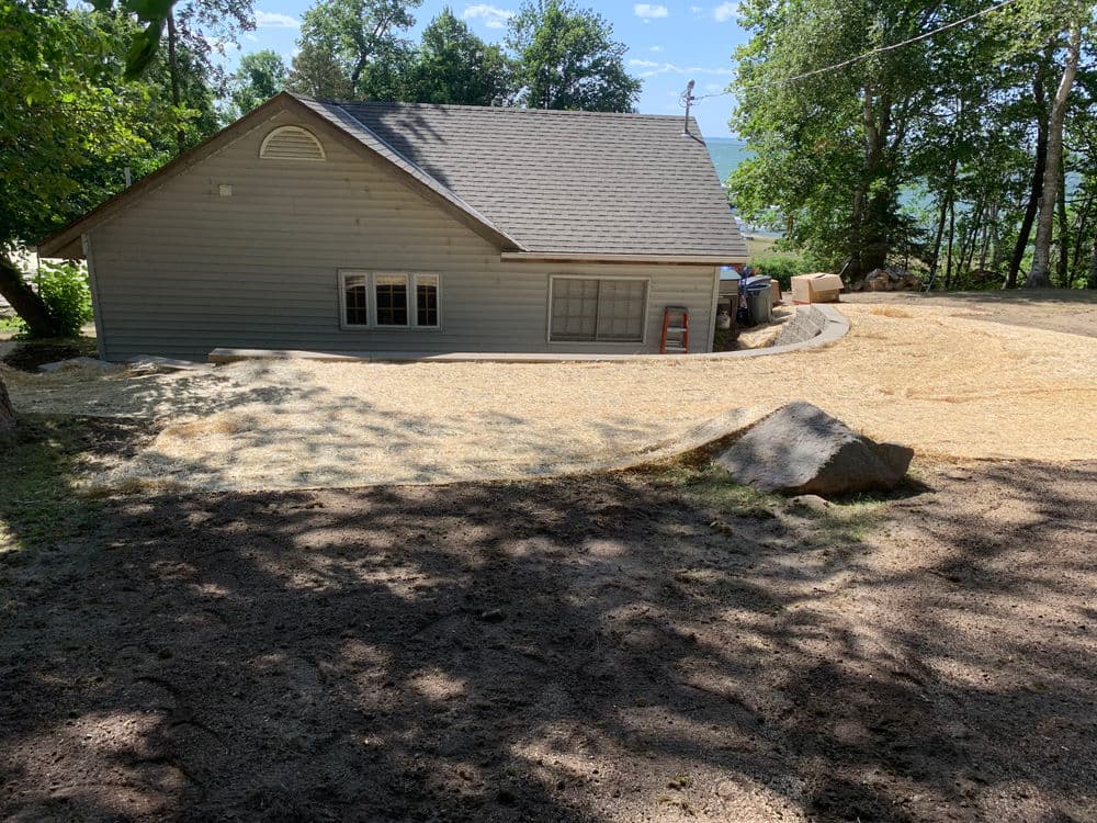 House with freshly spread mulch and landscaping under sunny skies in a wooded area.