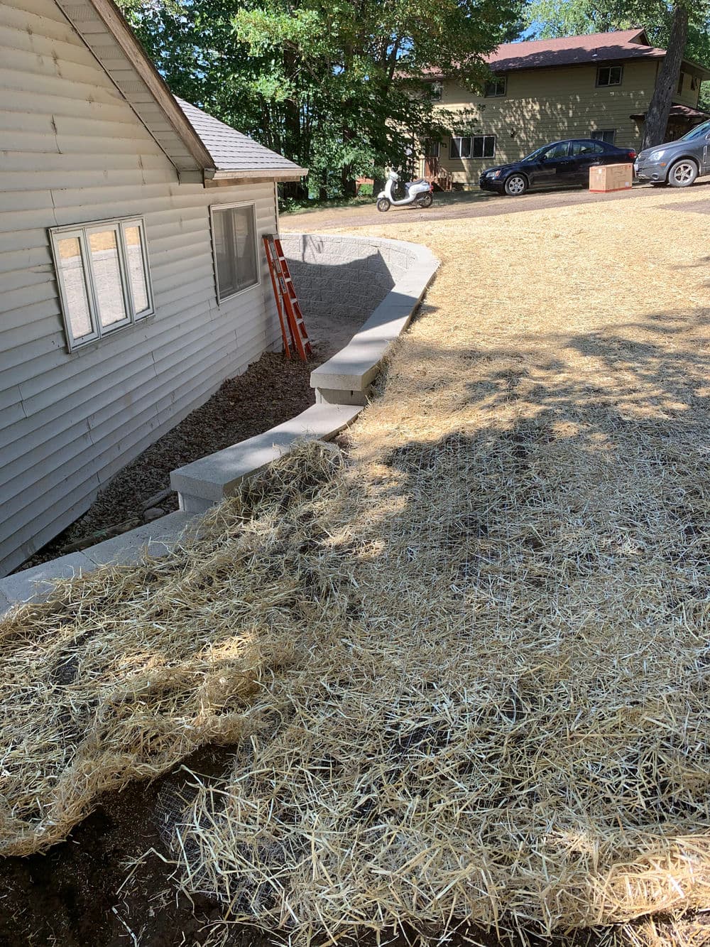 Residential landscape featuring a sloped yard, straw covering, and concrete steps.