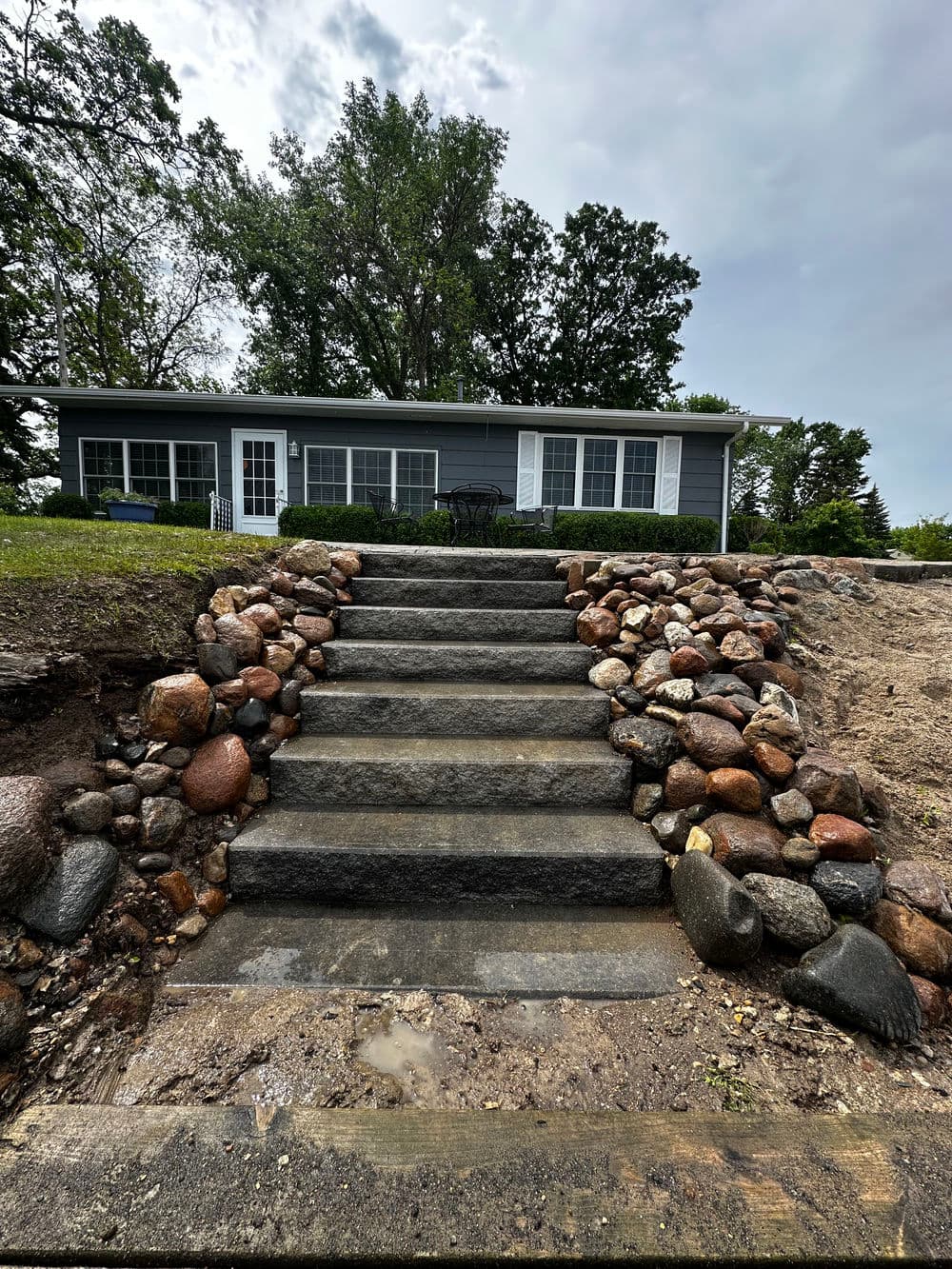 Stone pathway leading to a gray house with large windows surrounded by greenery.