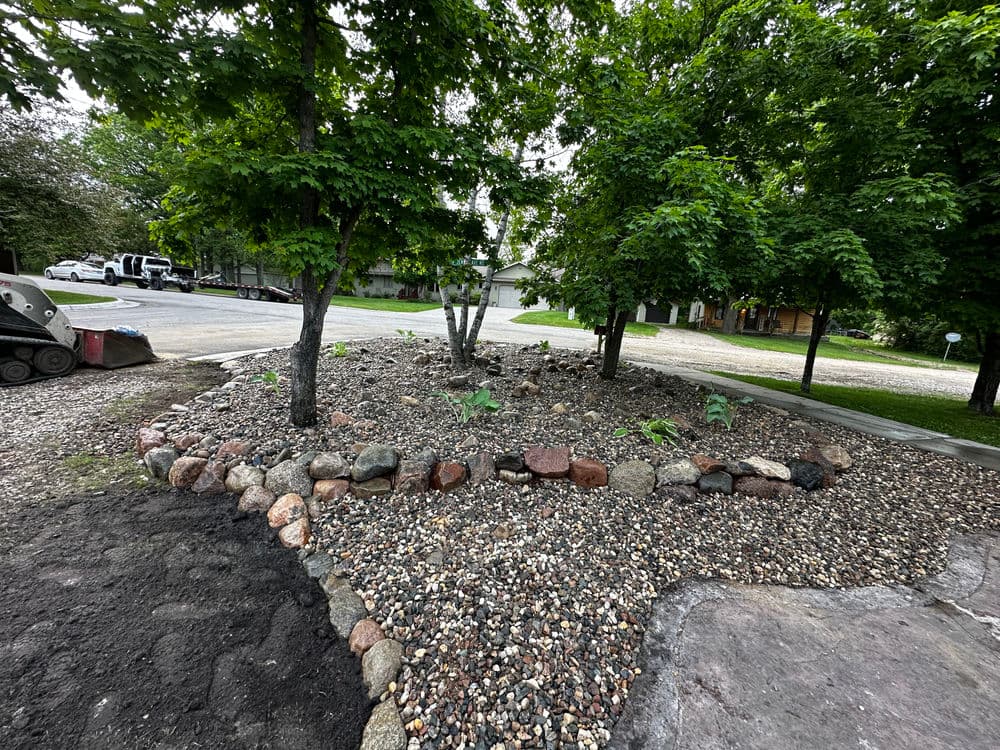 Landscaped garden area featuring stones, gravel, and healthy trees in a residential setting.
