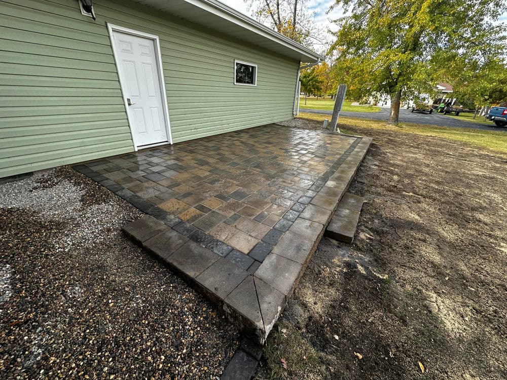 Newly installed paver patio next to a green house, featuring a clean and modern design.