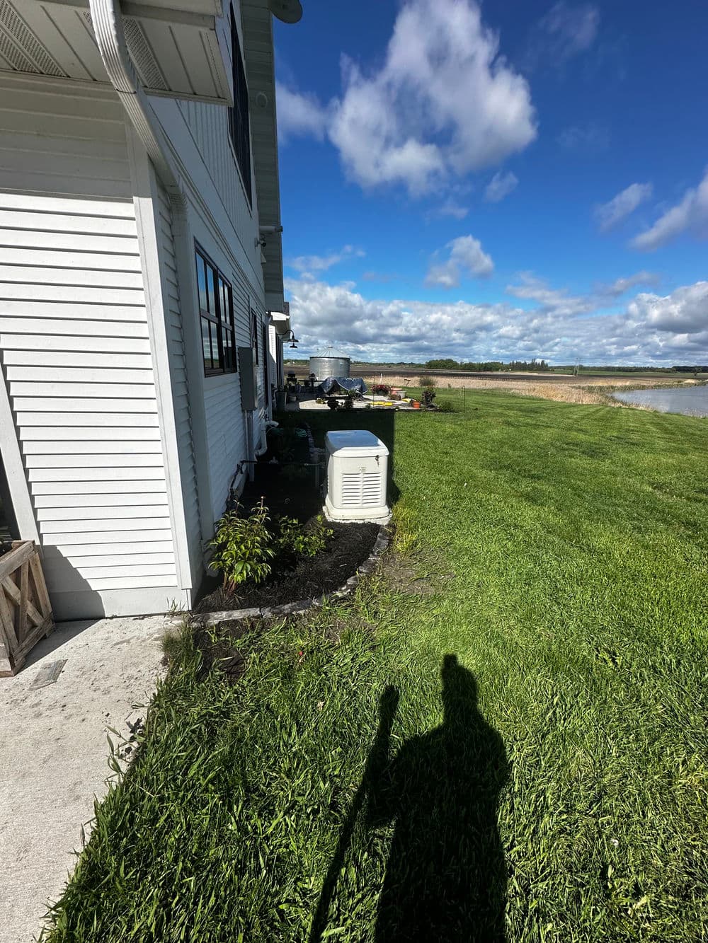 Air conditioning unit beside a house, with lush green grass and blue sky in the background.