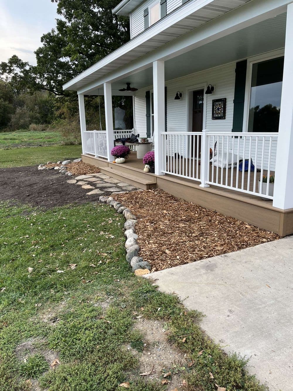 Charming porch with white railing, flower pots, and stone path leading to a landscaped yard.