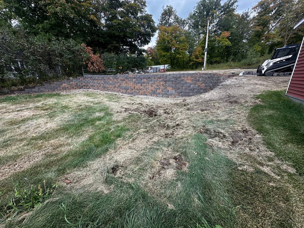 Newly landscaped backyard featuring a stone wall and freshly cut grass with construction equipment nearby.