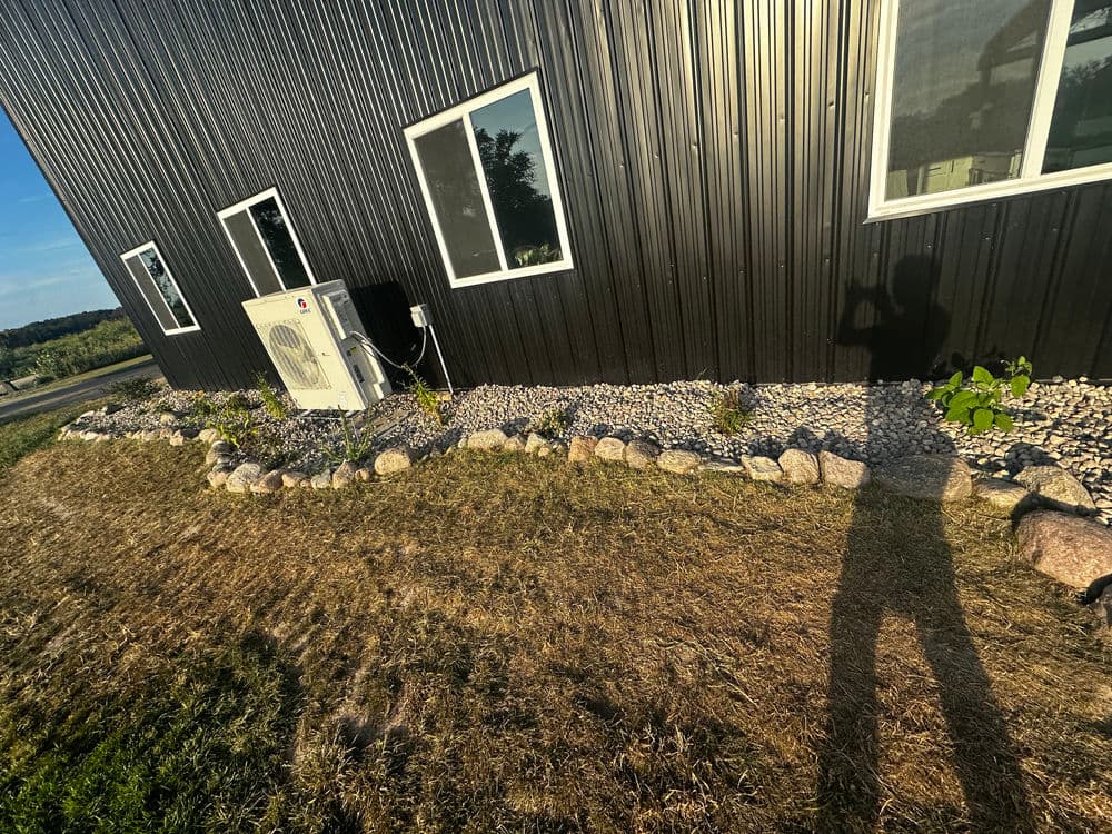 Modern black metal building with a gravel landscape, air conditioning unit, and shadow.