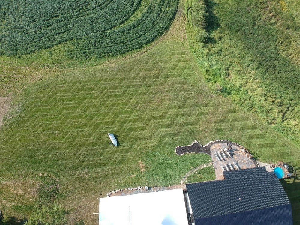 Aerial view of a patterned green lawn with a pool and patio area in a rural setting.
