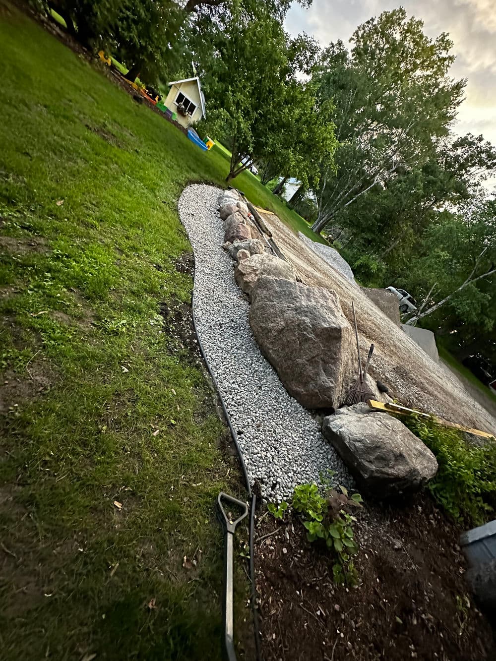 Landscaped garden featuring a gravel path lined with large rocks and lush green grass.