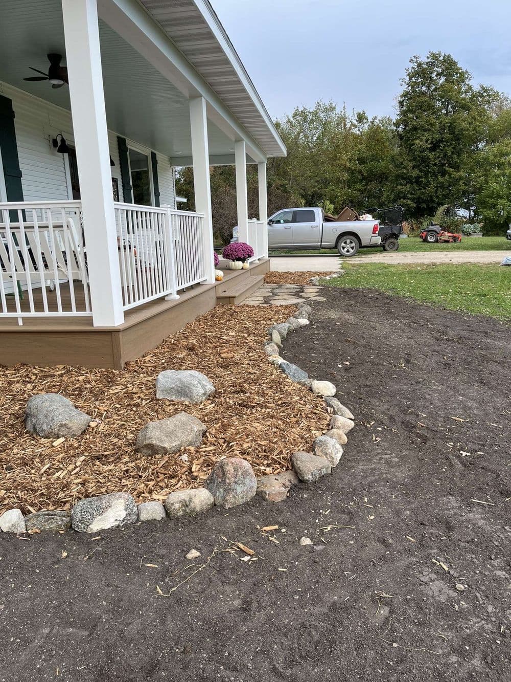 Renovated porch with wooden steps, landscaping rocks, and mulch in a yard setting.