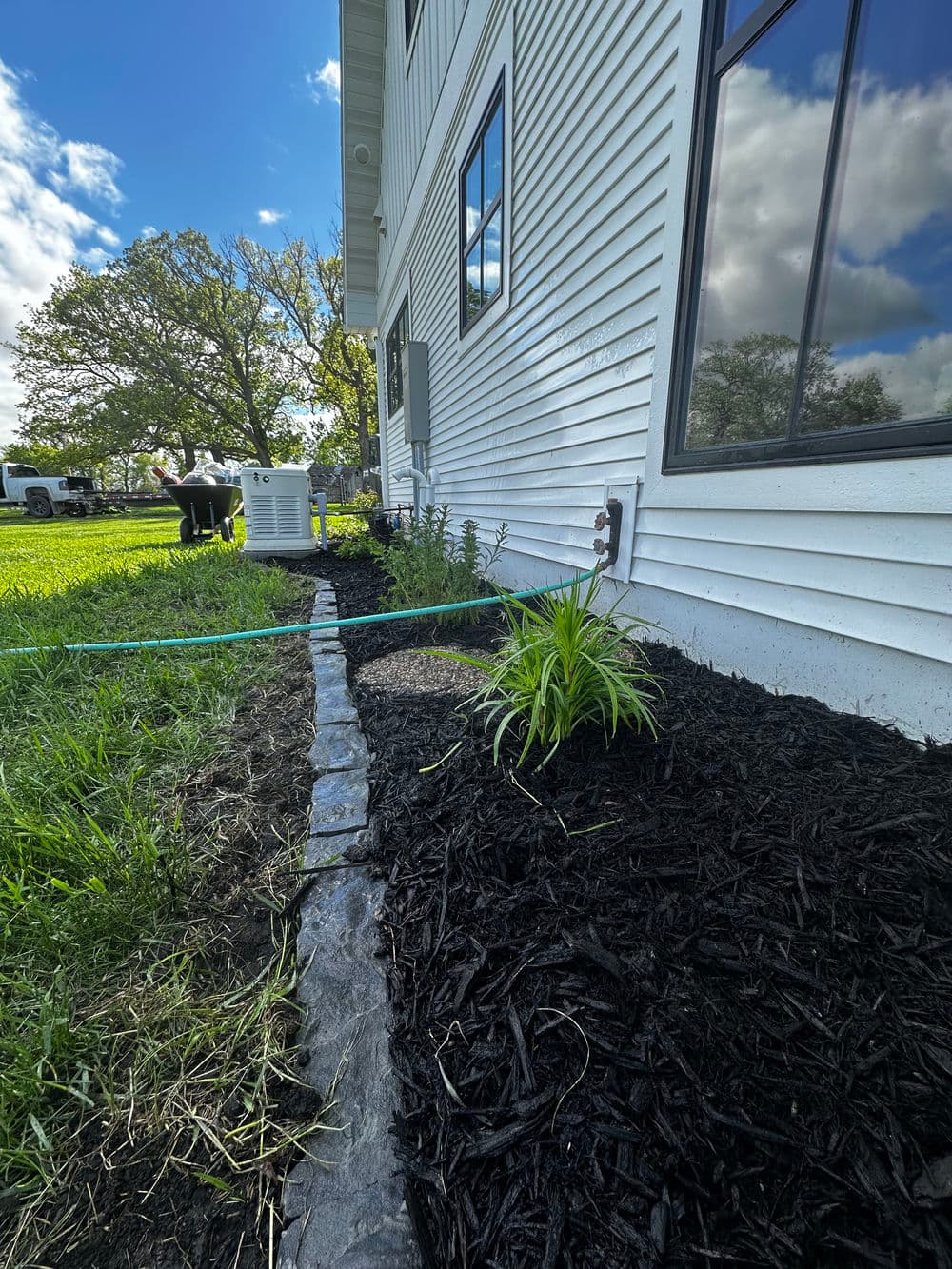 landscaped garden with mulch, plants, and a home exterior against a blue sky and clouds