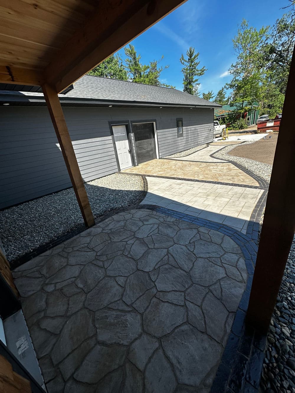 View of a modern stone pathway and gray house exterior with a clear blue sky.