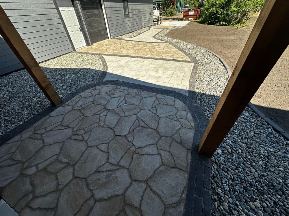 Decorative stone pathway with patio, bordered by gravel and greenery, leading to building entrance.
