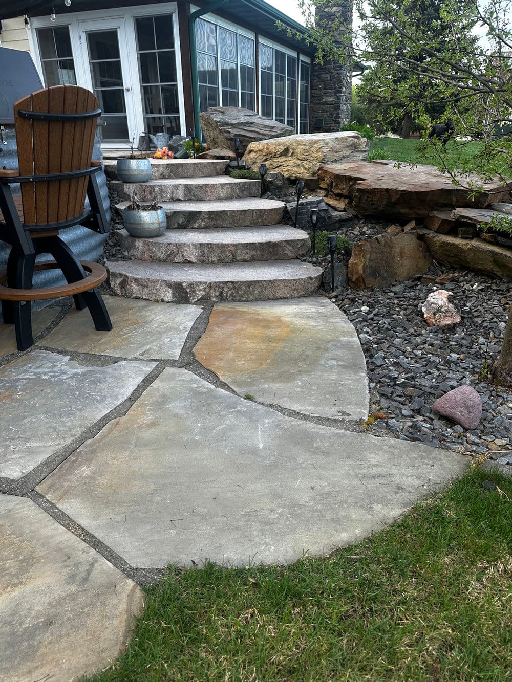 Stone steps leading to a patio, surrounded by natural stone features and green grass.