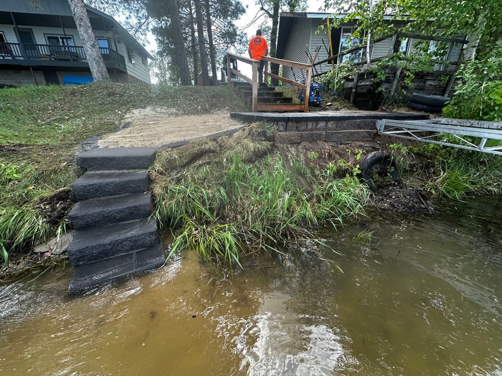Man in an orange vest standing near a newly constructed lakeside pathway and steps.