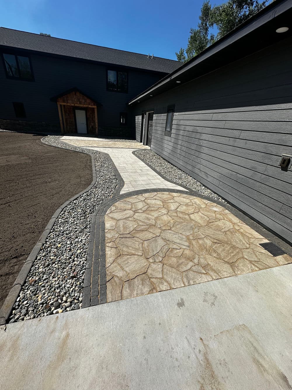 Stylish stone pathway leading to modern gray house with landscaped yard.