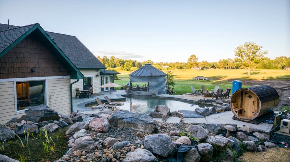 Scenic backyard oasis with a pool, sauna, and outdoor seating on a sunny day.
