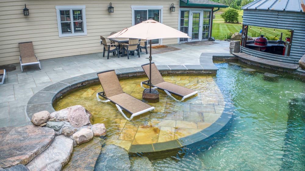 Luxury backyard with a pool, lounge chairs, and patio dining area under an umbrella.