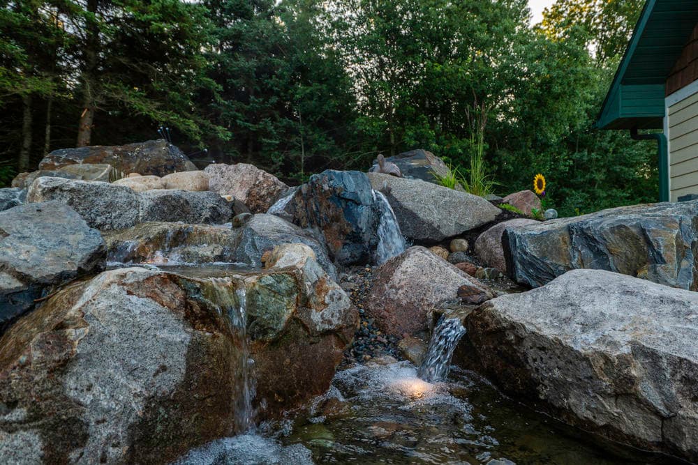 Scenic garden water feature with rocks and waterfall surrounded by lush greenery.