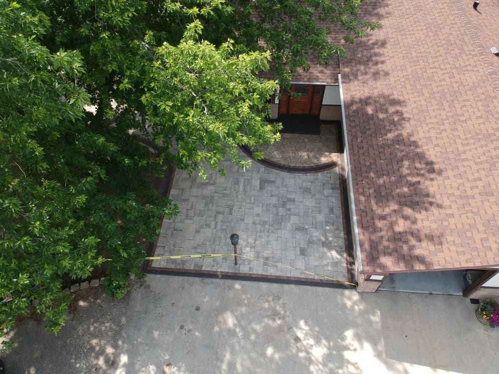 Aerial view of a home featuring a paved patio area and lush green trees nearby.