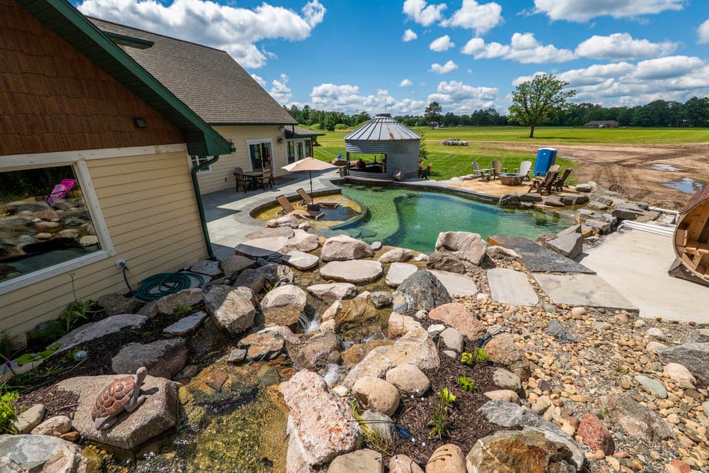 Scenic backyard with a modern pool, stone landscape, and gazebo under a blue sky.