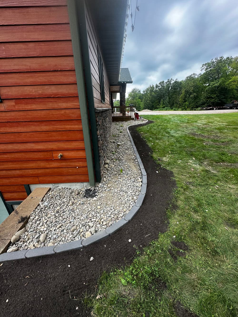 Landscaped garden section with gravel and edging beside a wooden house and grassy area.