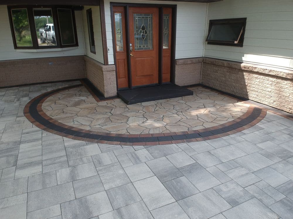 Stylish stone patio entrance with patterned design and wooden door, enhancing curb appeal.