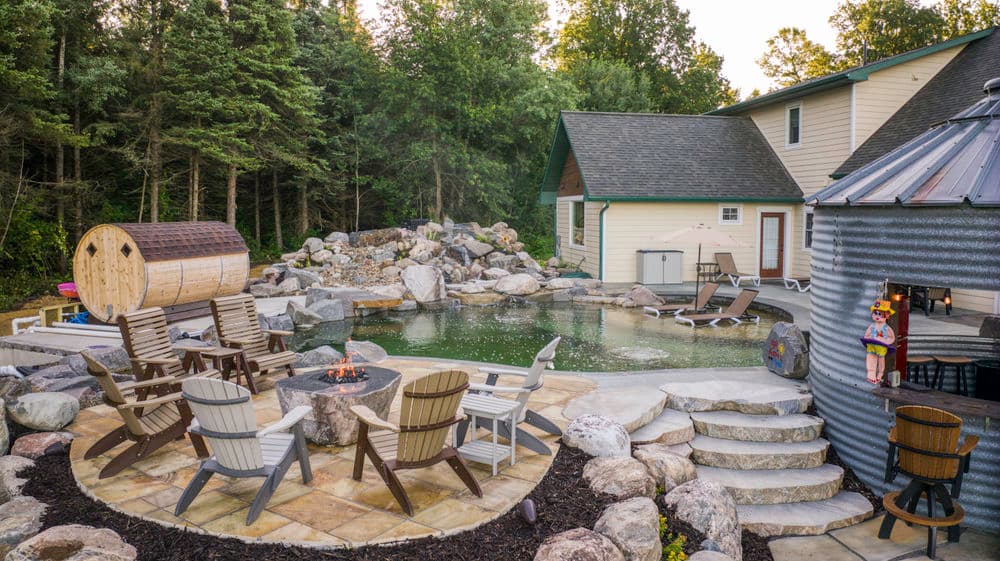 Backyard oasis featuring a stone pool, wooden chairs, and a sauna surrounded by trees.