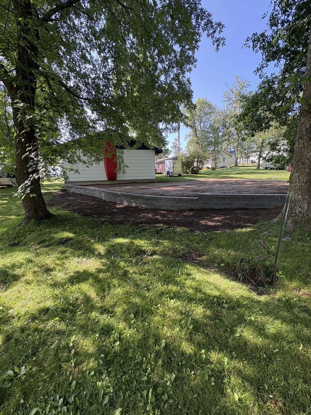 Home backyard with newly constructed patio, surrounded by trees and green grass on a sunny day.