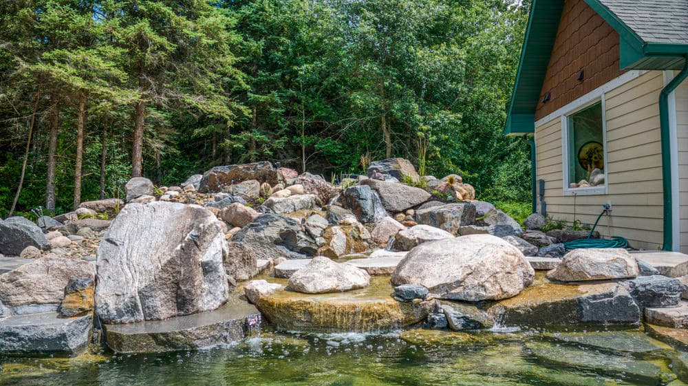 Water feature with large rocks near a cabin surrounded by lush greenery.