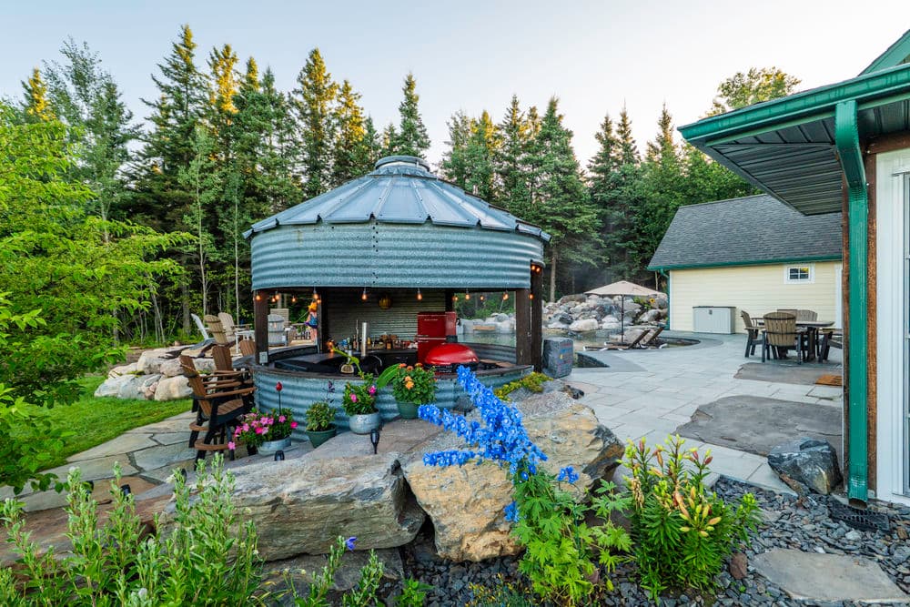 Rustic outdoor gazebo surrounded by blooming flowers and trees in a serene garden setting.