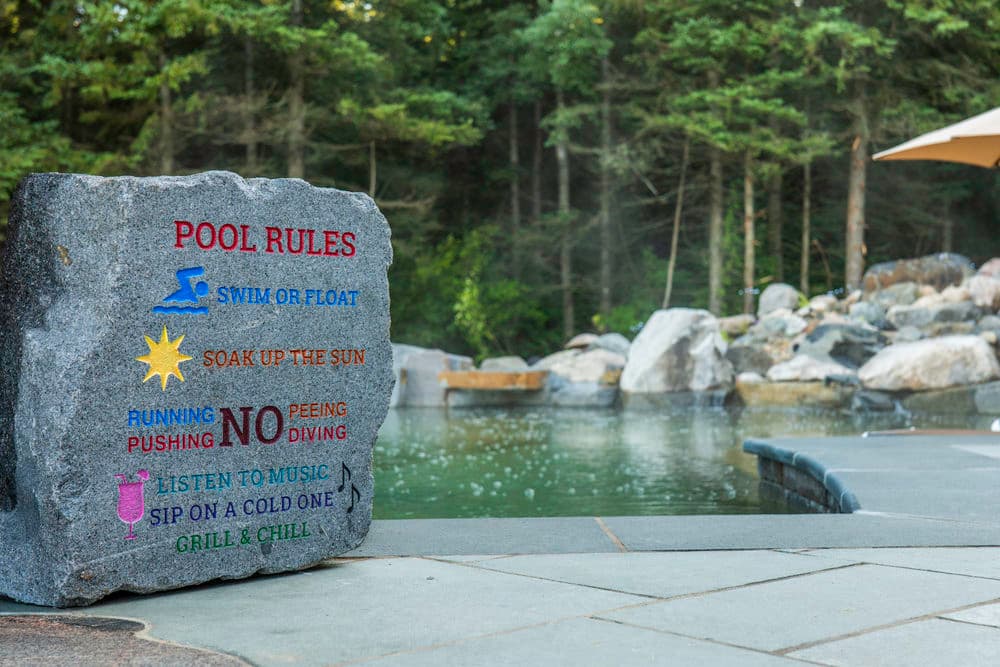Stone sign with pool rules: swim, sunbathe, no running or diving, enjoy music and drinks.