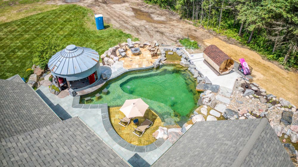 Aerial view of a luxurious backyard with a pool, spa, stone patio, and gazebo.