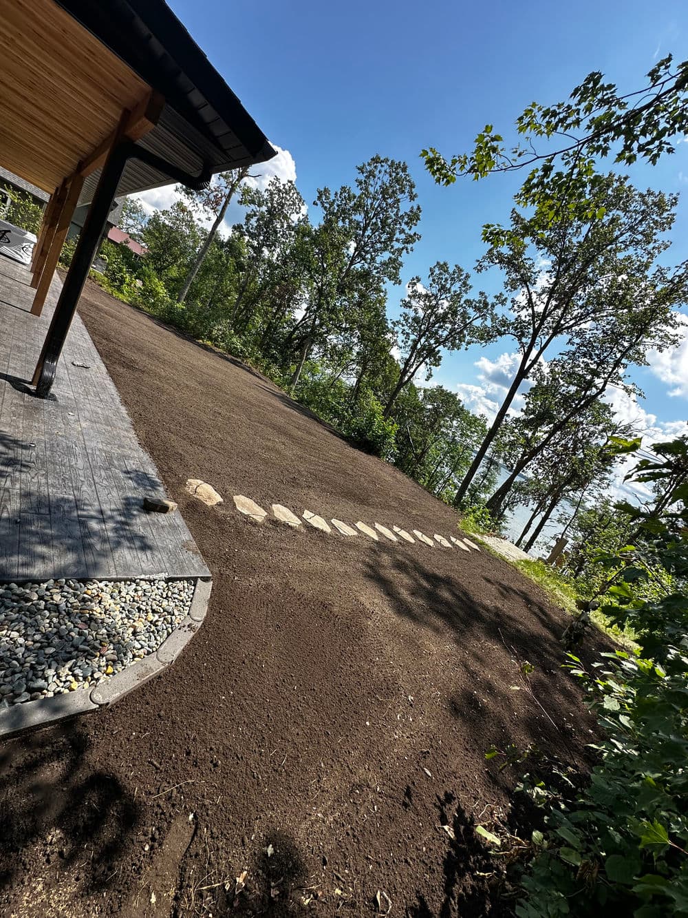 Landscaped outdoor area with gravel path, surrounded by trees and blue sky.
