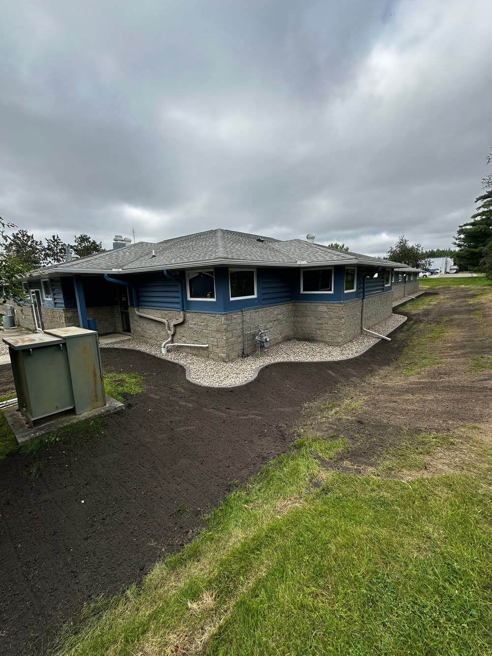 Blue house with stone accents, new landscaping, cloudy sky in the background.
