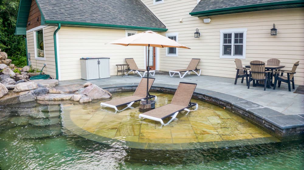 Backyard oasis with a pool, lounge chairs, umbrella, and patio dining set near a house.